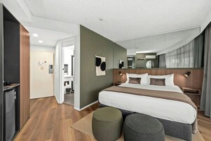 Ett modernt hotellrum med en stor säng, sängbord, en spegel och utsikt över korridoren.