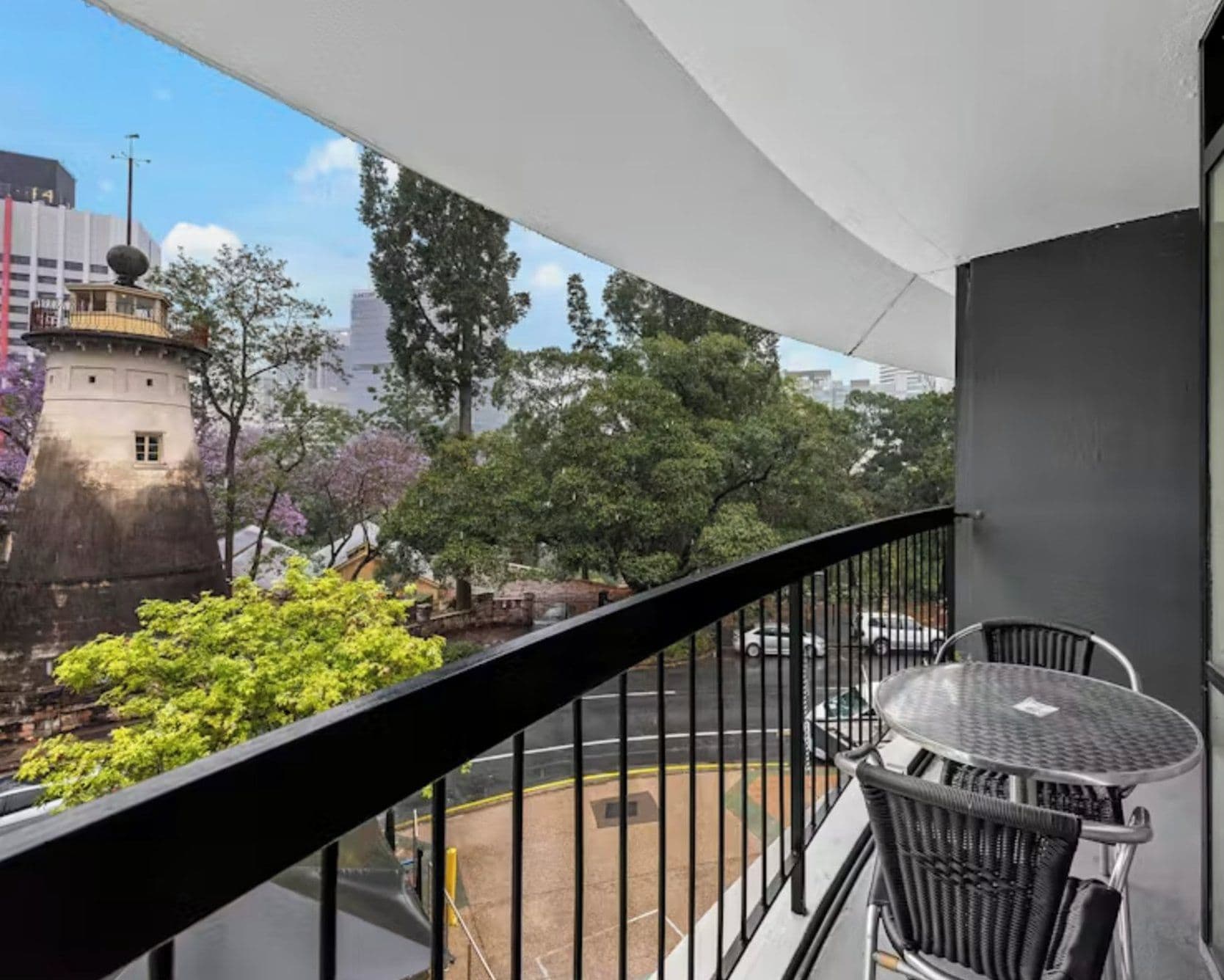 A balcony with a view of a tower, trees, and a parking lot.