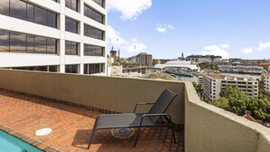 Eine Dachterrasse mit Backsteinboden, einem einzelnen schwarzen Liegestuhl und Blick auf eine Skyline mit Gebäuden und einem Yachthafen.