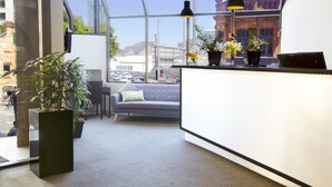 Ein moderner Empfangsbereich mit einer Couch, Topfpflanzen und Blick auf die Stadt durch große Fenster.