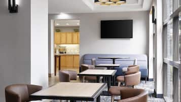 Un comedor moderno con cocina al fondo, un televisor de pantalla plana montado en la pared y un conjunto de mesas y sillas.