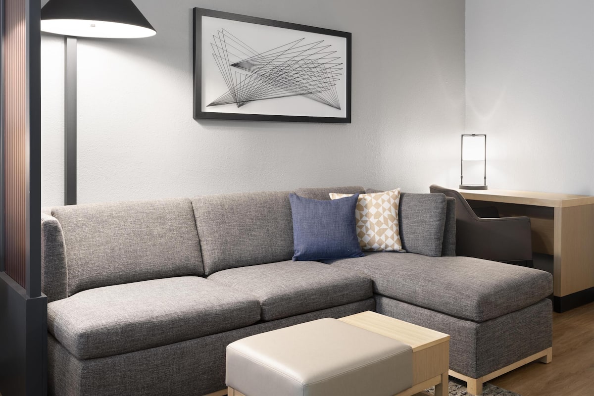 A modern living room with a grey sectional sofa, a small wooden table, and a desk with a lamp.
