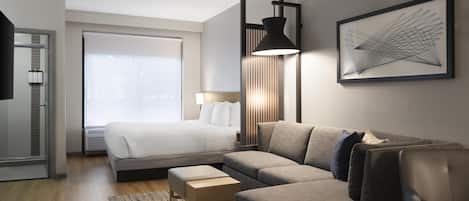 A modern hotel room with a bed, a sofa, a desk, and a large window.