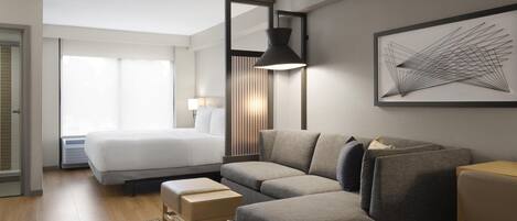 Una habitación de hotel moderna con una cama grande, un sofá gris, una mesita pequeña y una lámpara fijada a la pared.