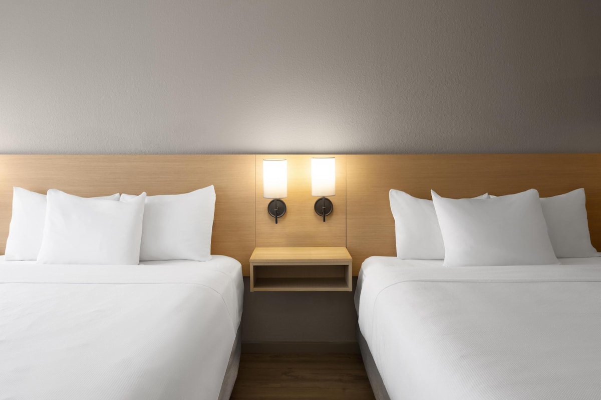 A hotel room with two beds, a wooden headboard, and a nightstand with a lamp.