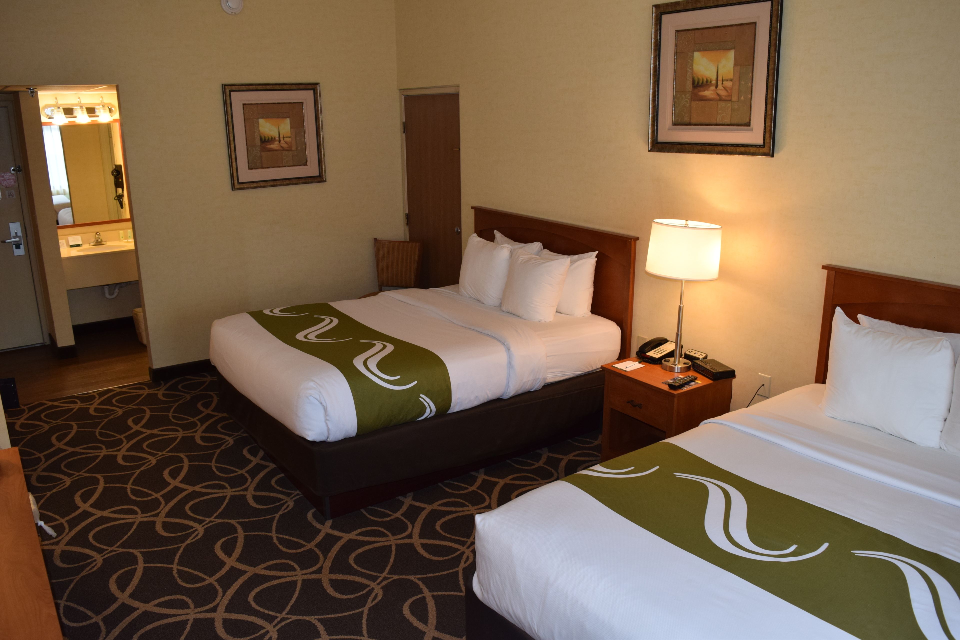 A hotel room with two beds, a bathroom, and a hallway.