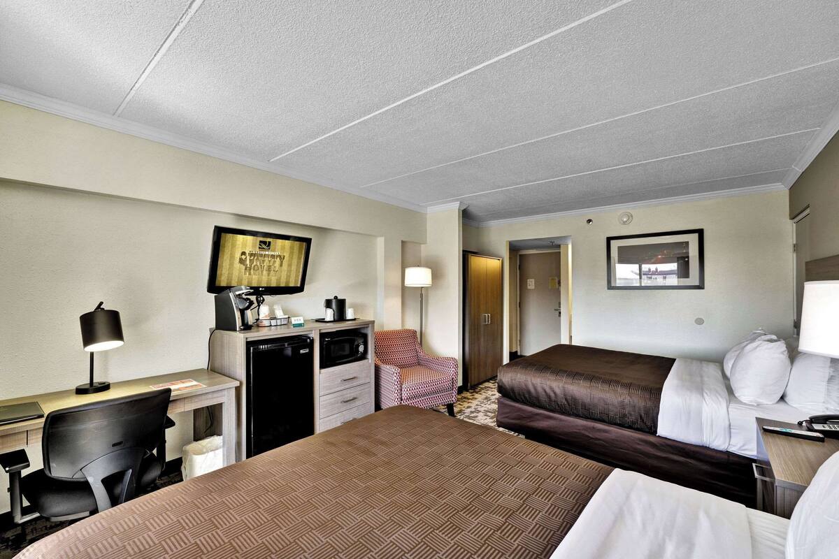 Une chambre d’hôtel avec deux lits, un bureau avec une lampe, une chaise, un petit coin cuisine et un tableau encadré au mur.