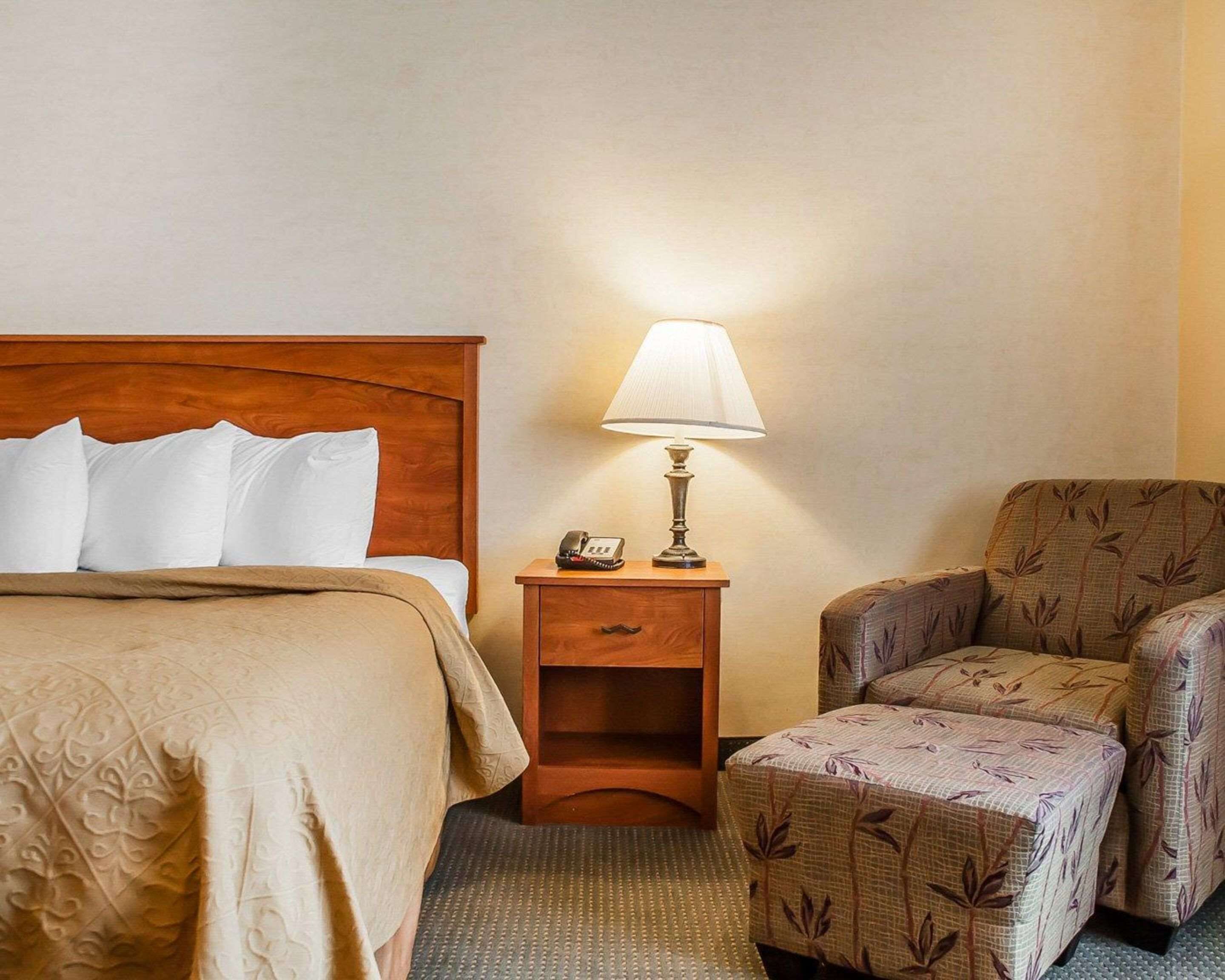 Een hotelkamer met een houten bed, een bedlampje, een telefoon en een fauteuil met een patroon.