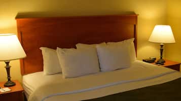 Une chambre d’hôtel avec une tête de lit en bois, un lit recouvert de draps blancs, deux lampes de chevet et un tableau encadré au mur.