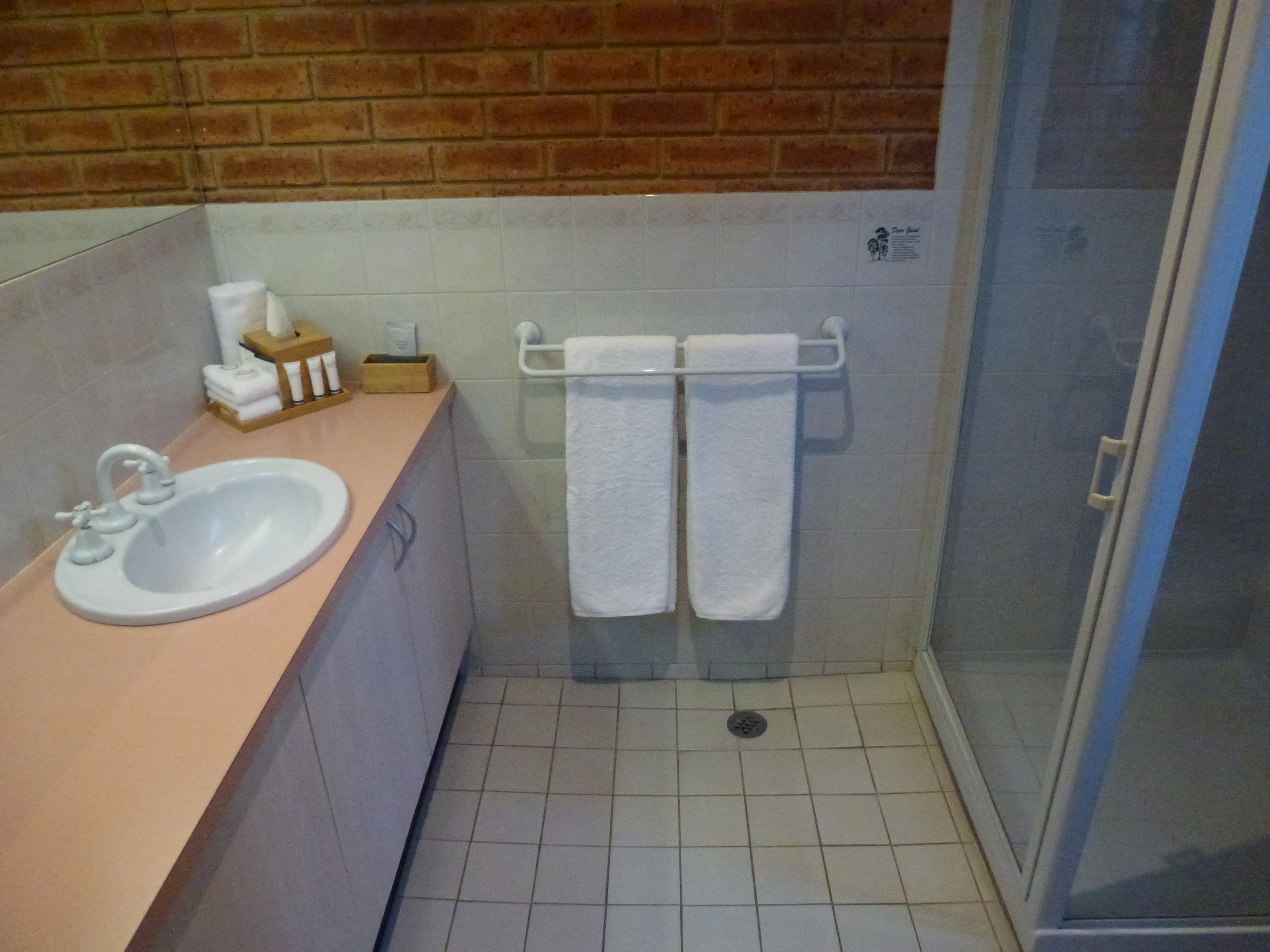 A bathroom with a sink, a towel rack with two towels, a shower area, and a small wooden box with toiletries.