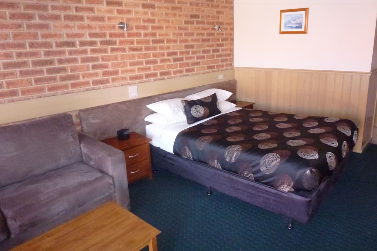A hotel room with a brick wall, a bed with a patterned bedspread, a grey sofa, and a small wooden table.