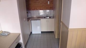 A compact kitchen with a refrigerator, sink, and tiled floor.