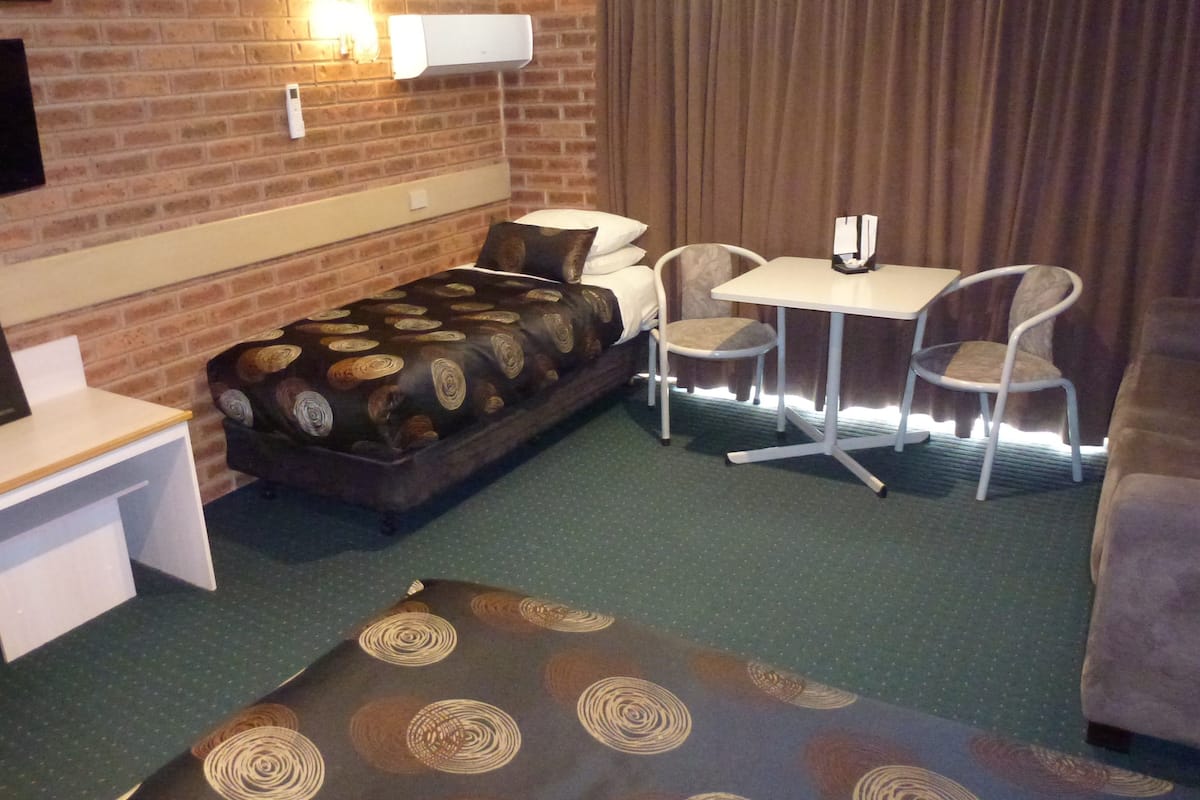 A hotel room with a bed, a desk, a chair, and a small table.