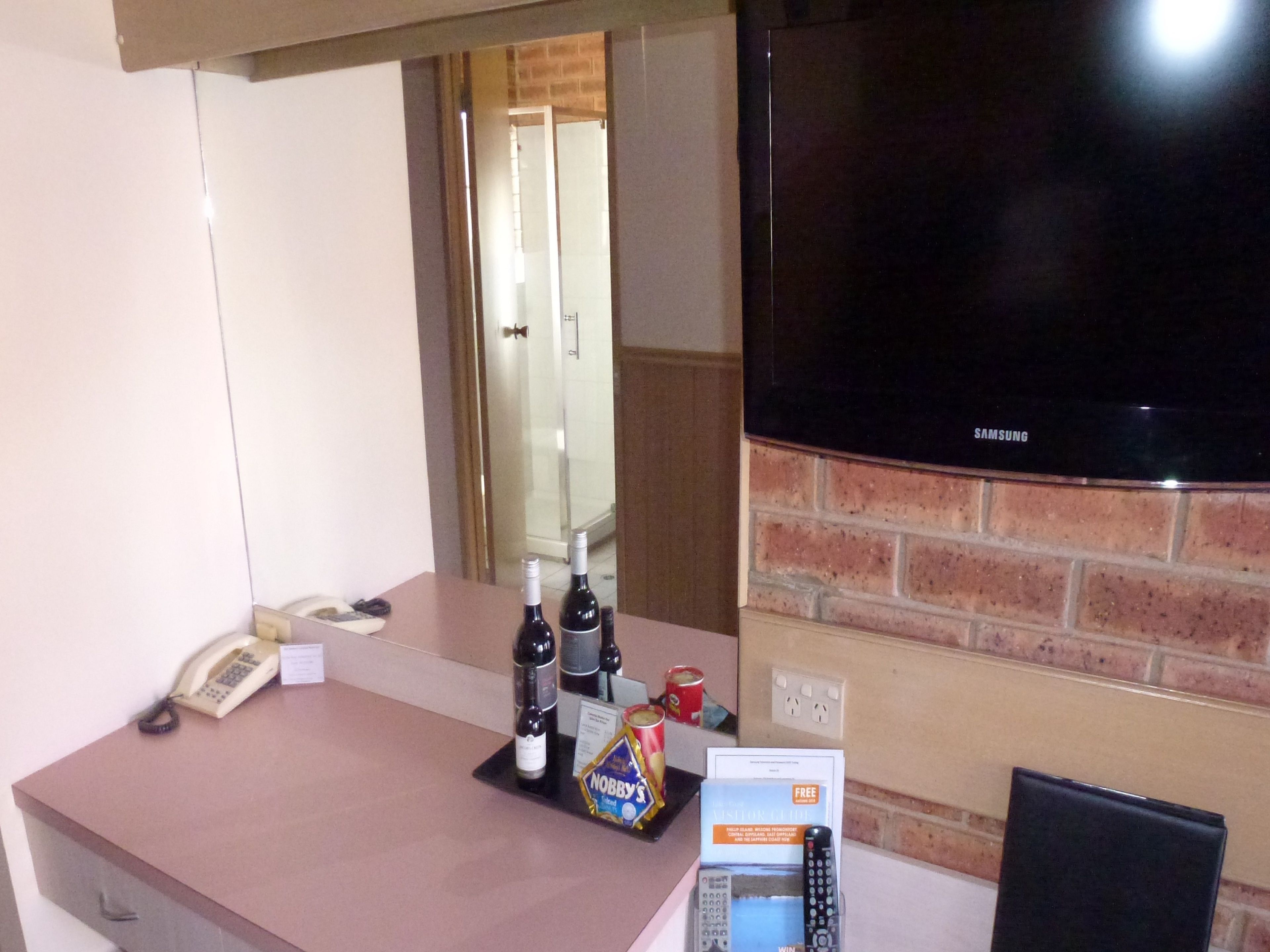 Un comptoir de réception d’hôtel équipé d’un téléviseur à écran plat, d’un téléphone et d’un mini-bar contenant des bouteilles de vin, des en-cas et une télécommande.