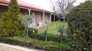 Uma casa de dois andares com telhado vermelho, fachada de tijolos e um pequeno jardim frontal com gramado e algumas árvores.