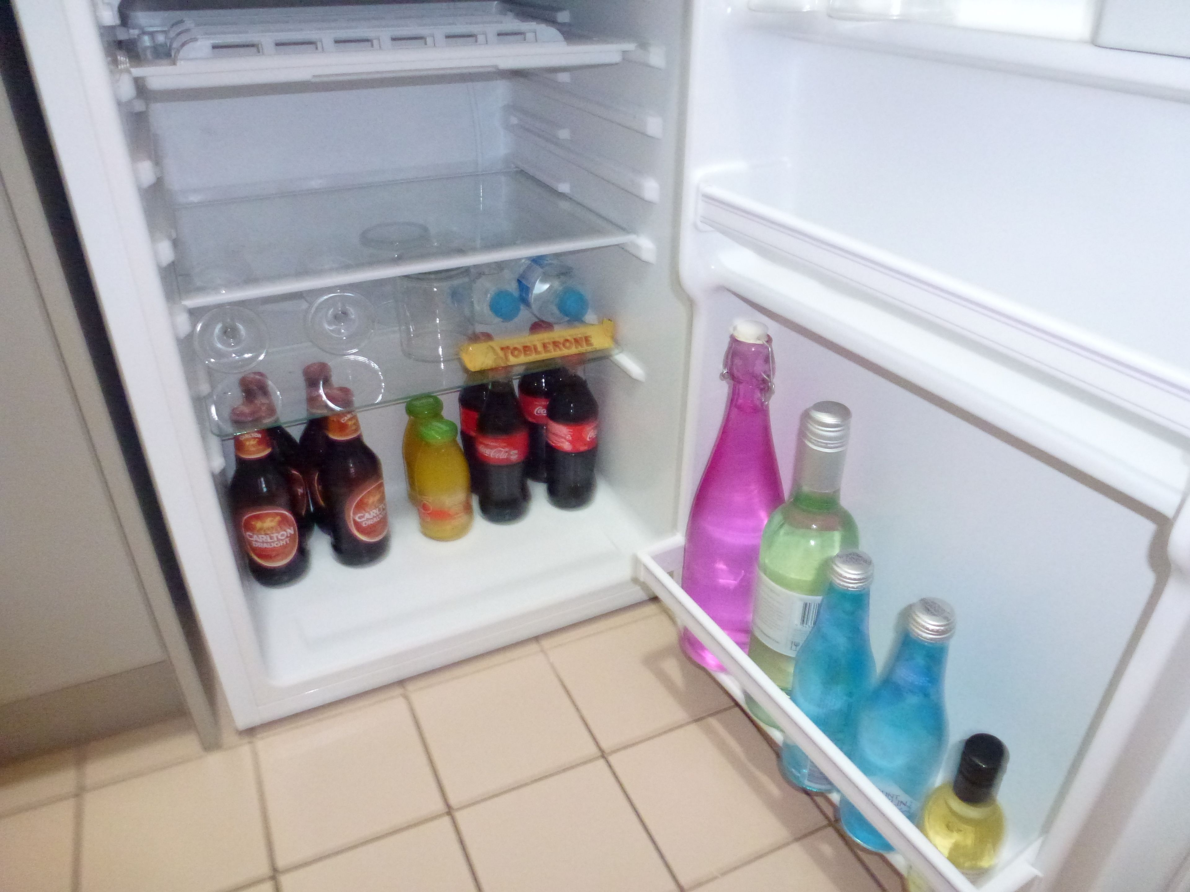 An open refrigerator with various bottles and containers, including bottles of Coca-Cola, a bottle of wine, and a bottle of water.