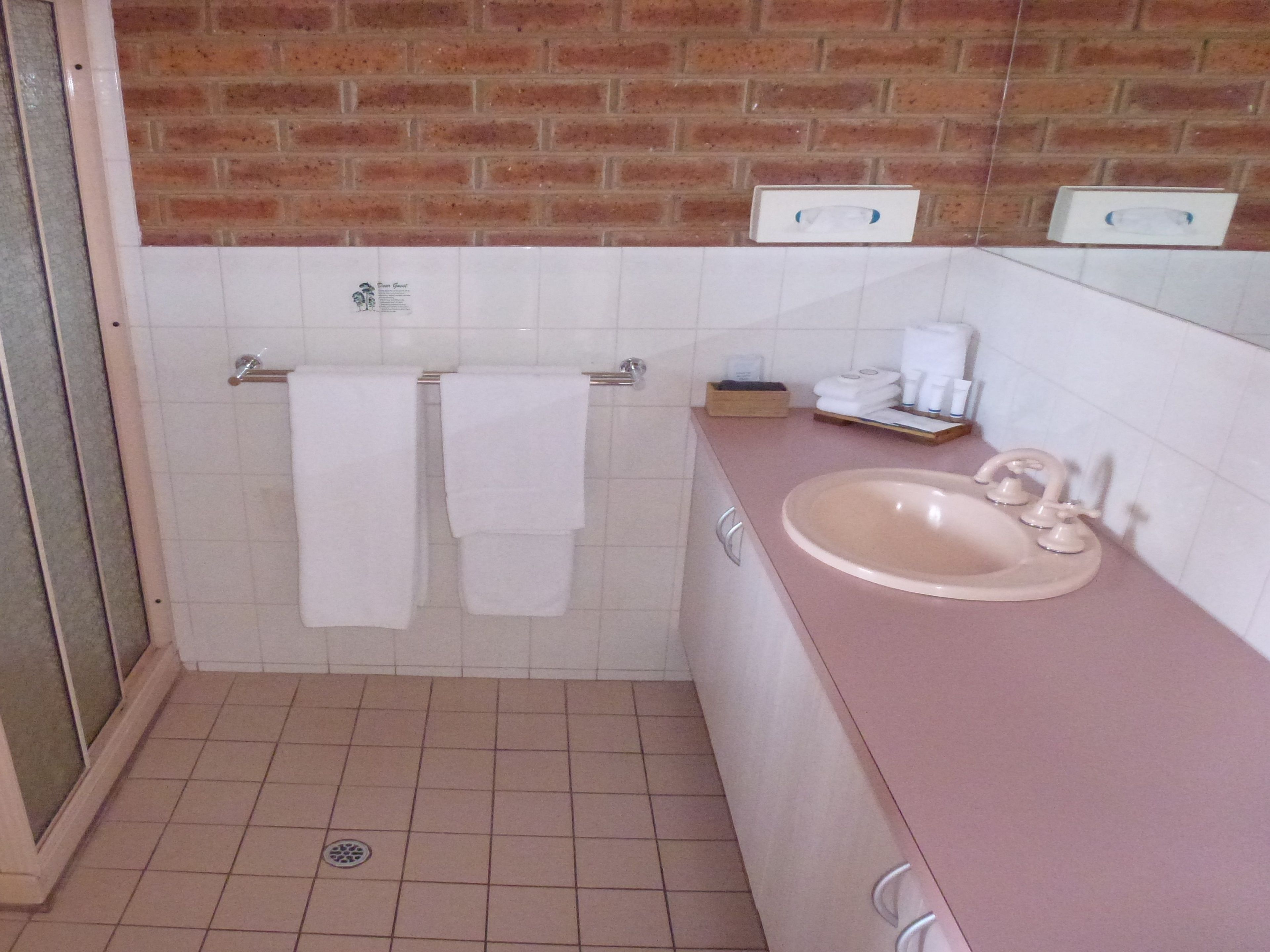 A bathroom with a pink sink, white tiles, and a brick wall.