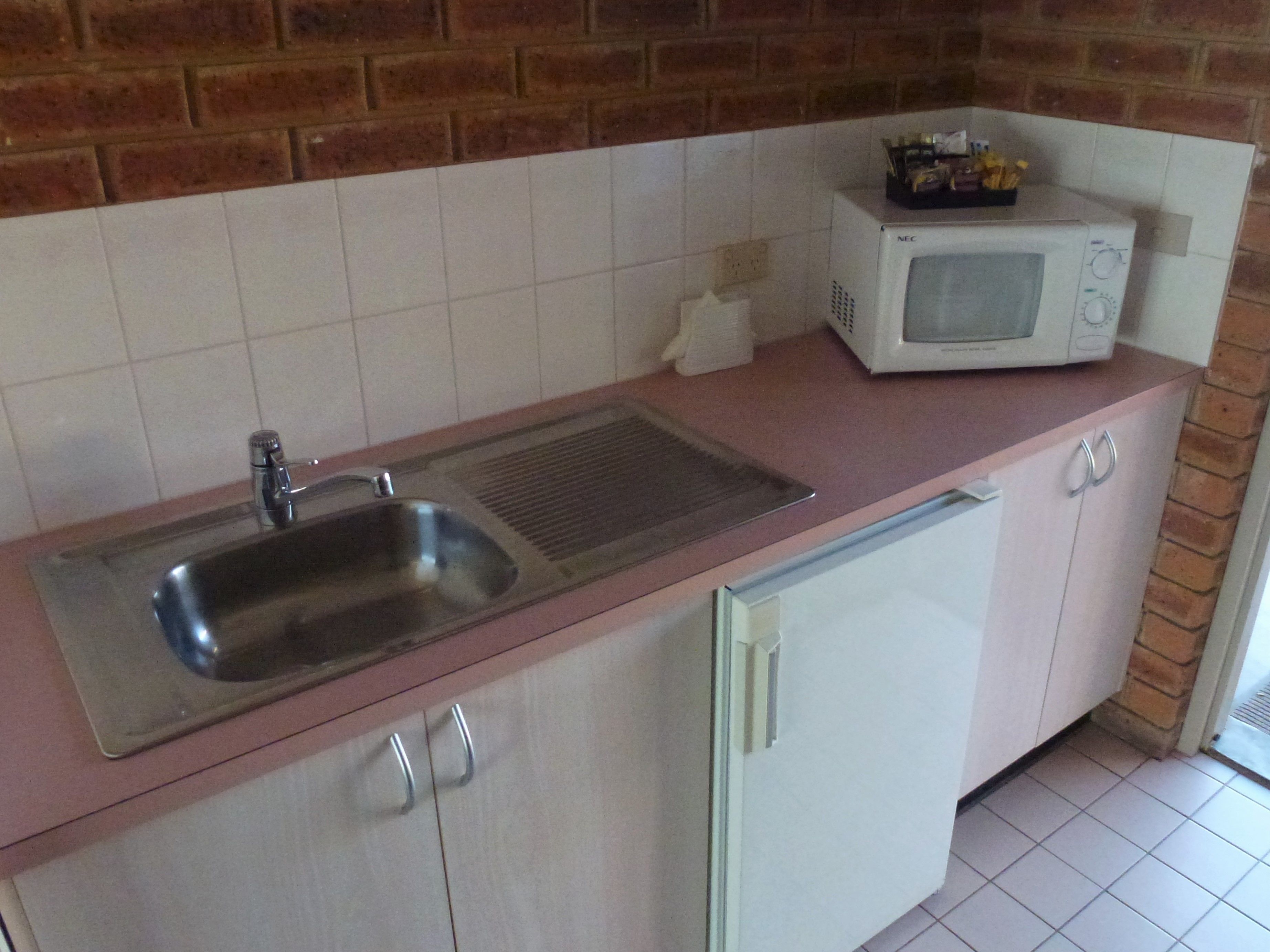 A kitchen with a stainless steel sink, a microwave, and a cabinet with two handles.