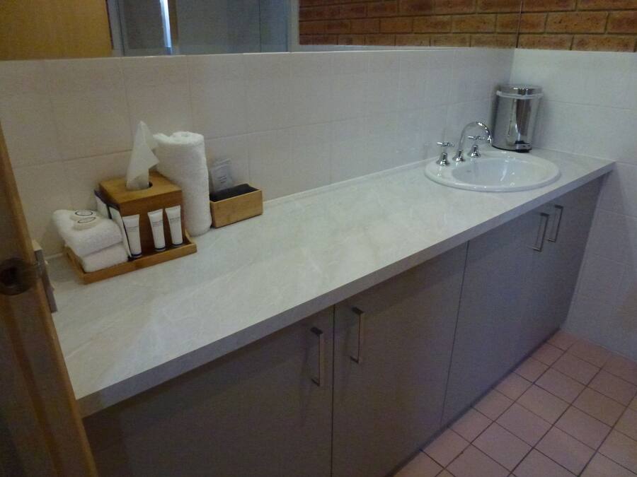 A bathroom with a white countertop, a sink, and a mirror. There are towels and toiletries on the counter.