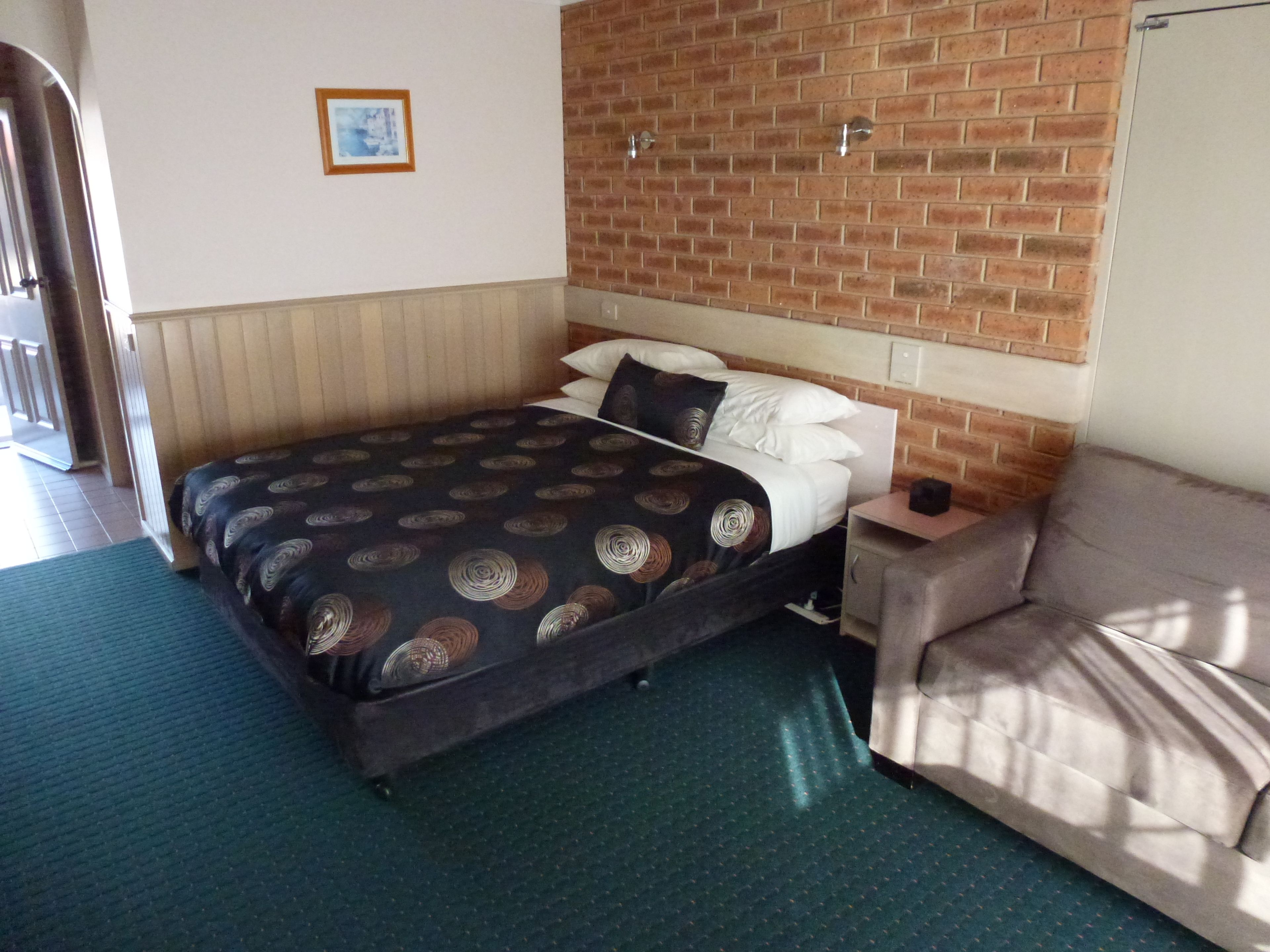 Una habitación de hotel con una cama, una mesita de noche, un sofá, una pared de ladrillo y un cuadro enmarcado en la pared.