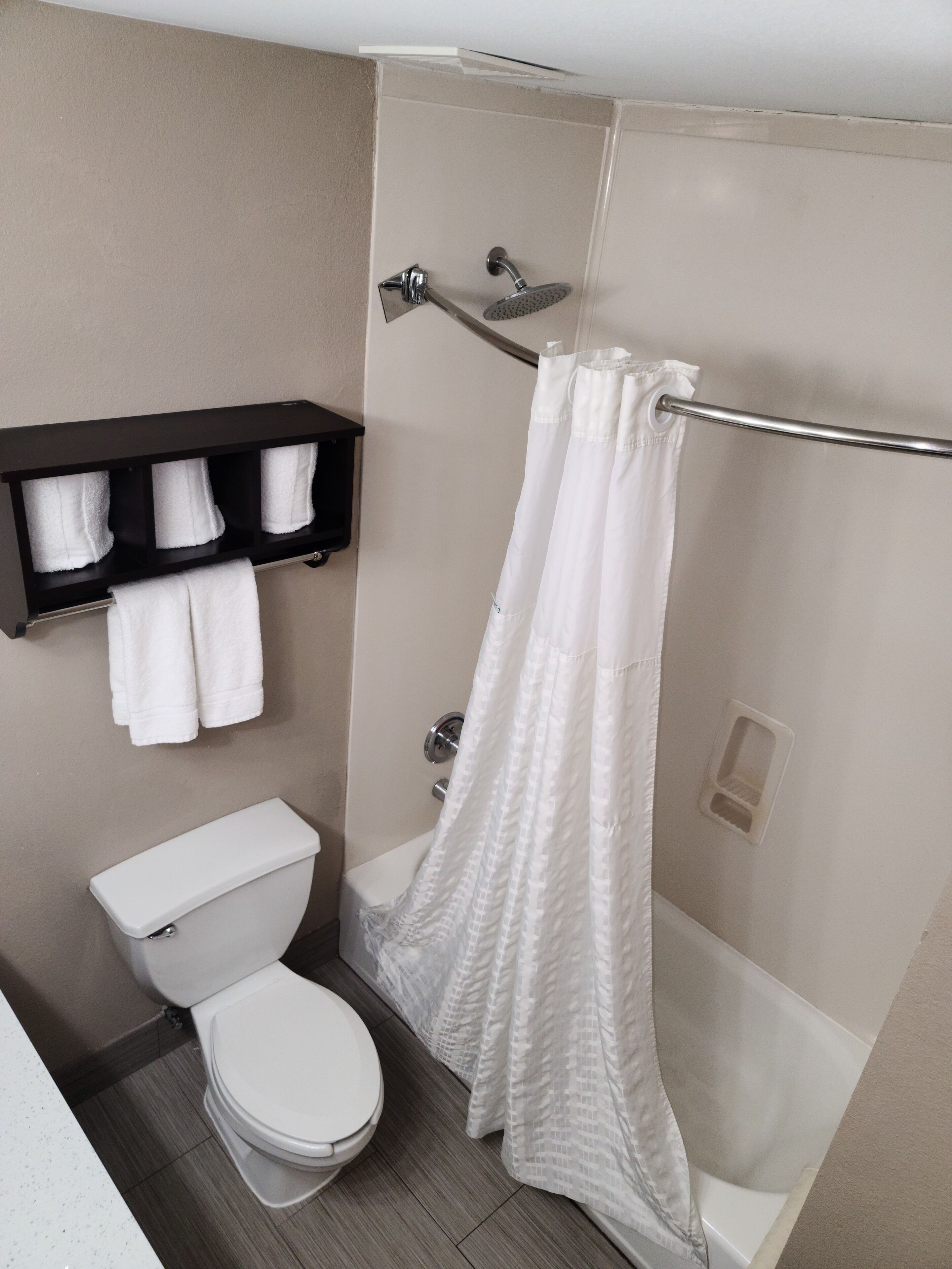 A bathroom with a toilet, a shower with a white shower curtain, and a towel rack with white towels.