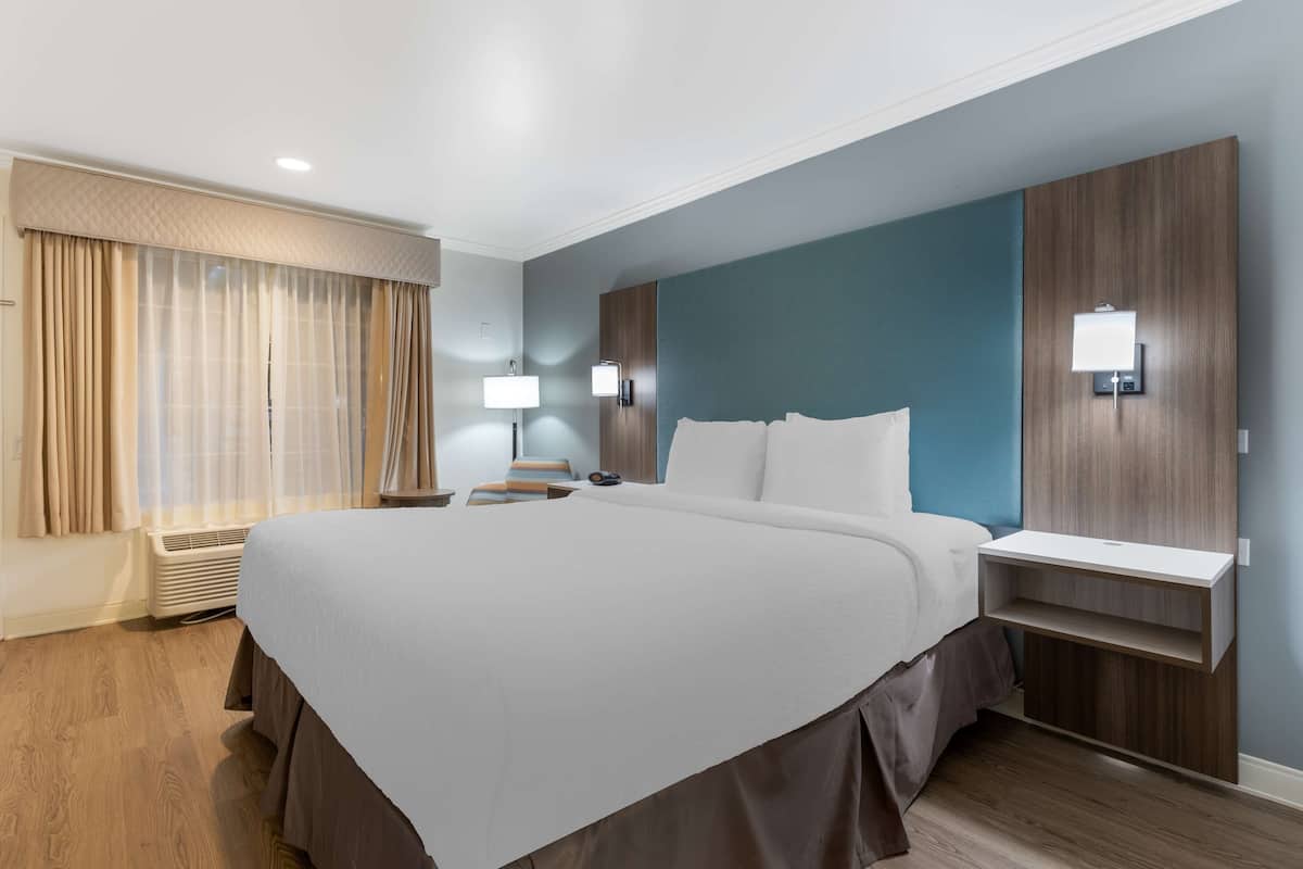 A hotel room with a large bed, bedside tables, a desk, and a window with curtains.