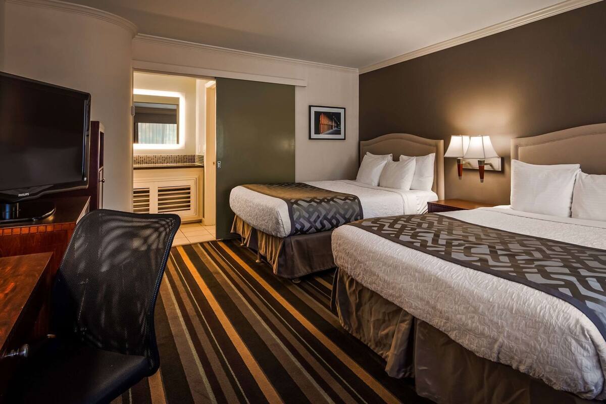 A hotel room with two beds, a television, a desk, and a chair.
