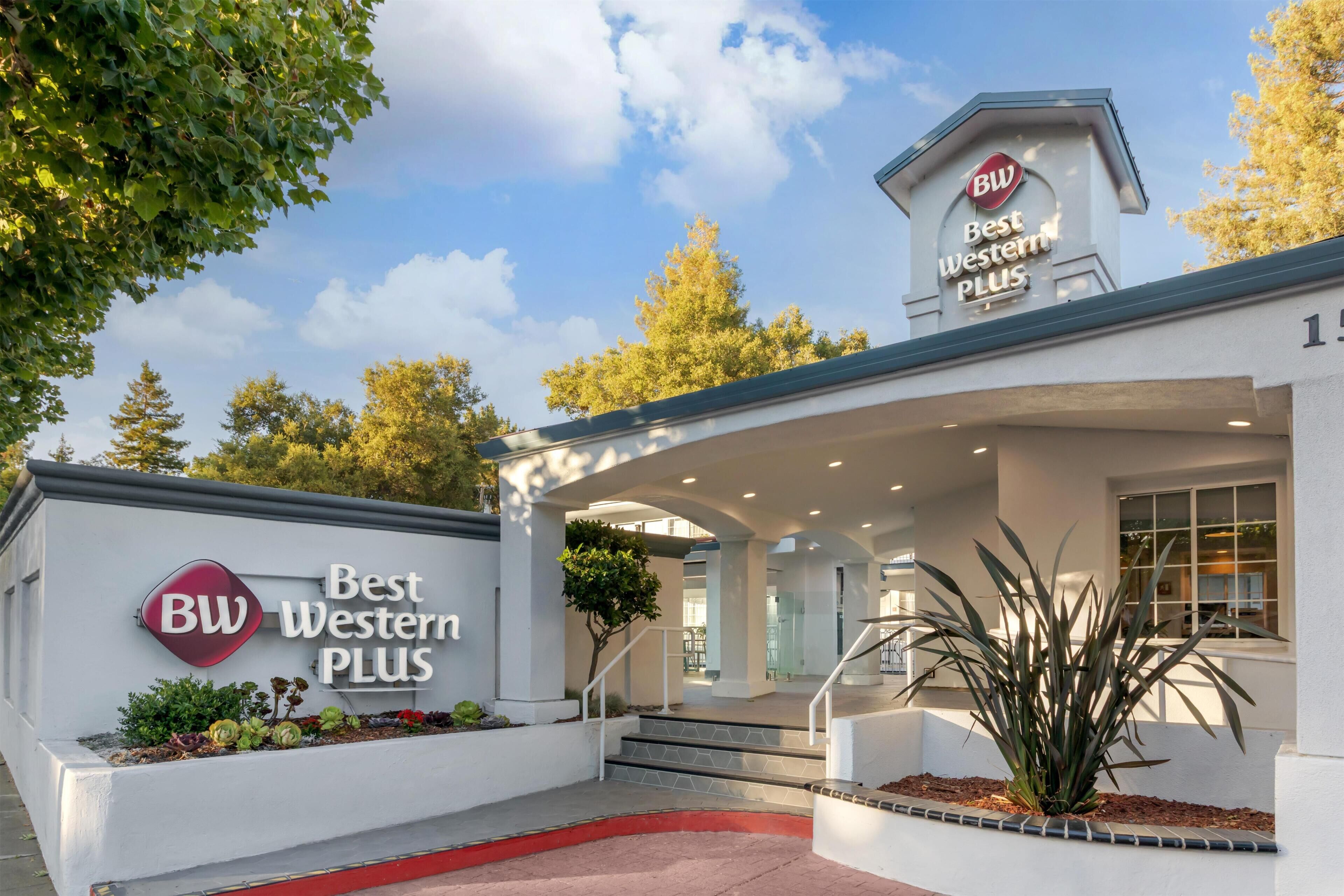 Fachada de un hotel Best Western Plus, con un área exterior cubierta, escalones que conducen a la entrada y un cielo despejado al fondo.