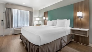 A hotel room with a large bed, a bedside table, a lamp, and a view of the city through the window. - Best Western Plus Riviera (Menlo Park)