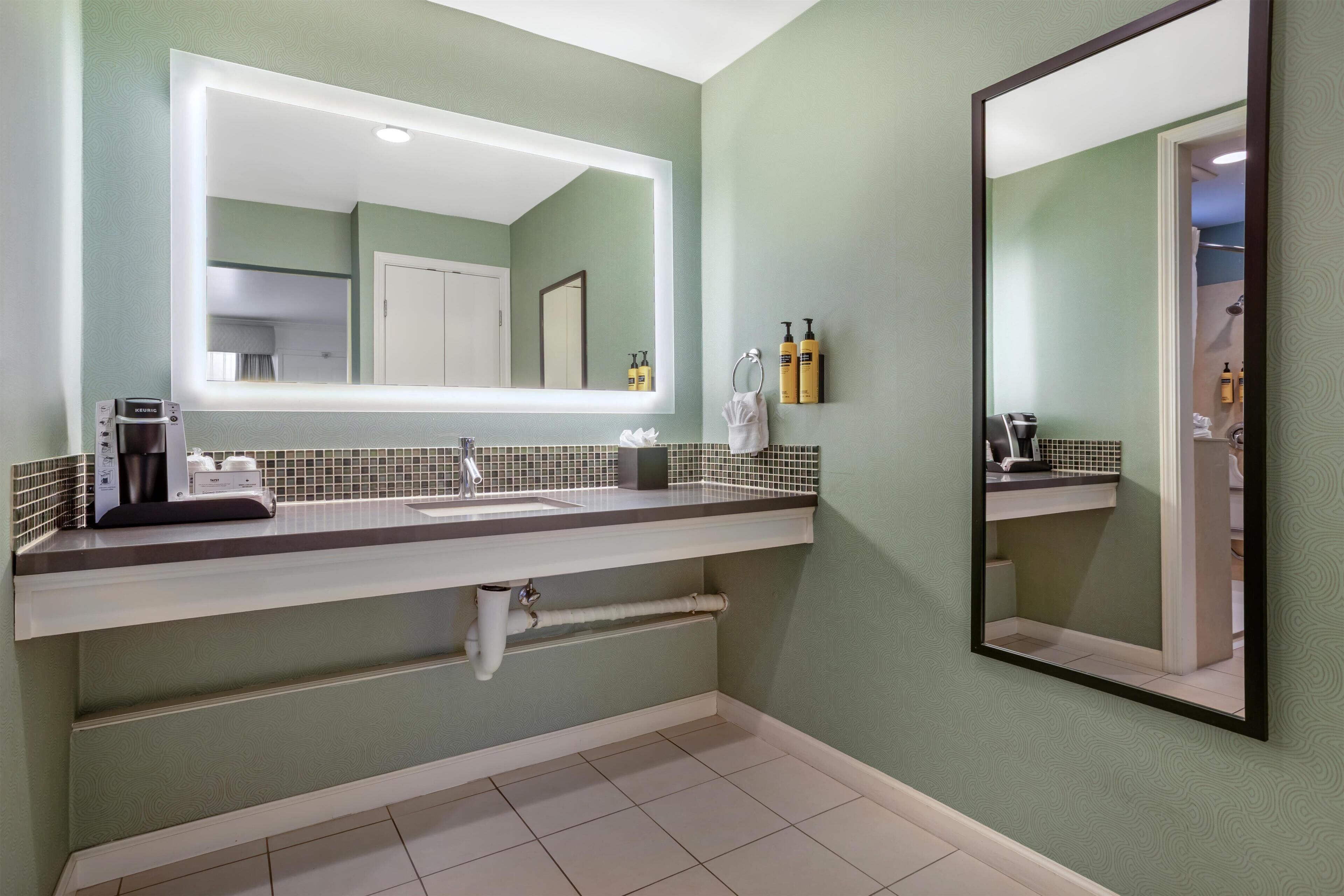 A bathroom with a large mirror, a coffee machine, and toiletries on the counter.
