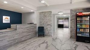 A reception area with a blue wall, a reception desk, a chair, a Coca-Cola refrigerator, and a stone wall. - Suburban Studios Hinesville - Fort Stewart Area (Hinesville)