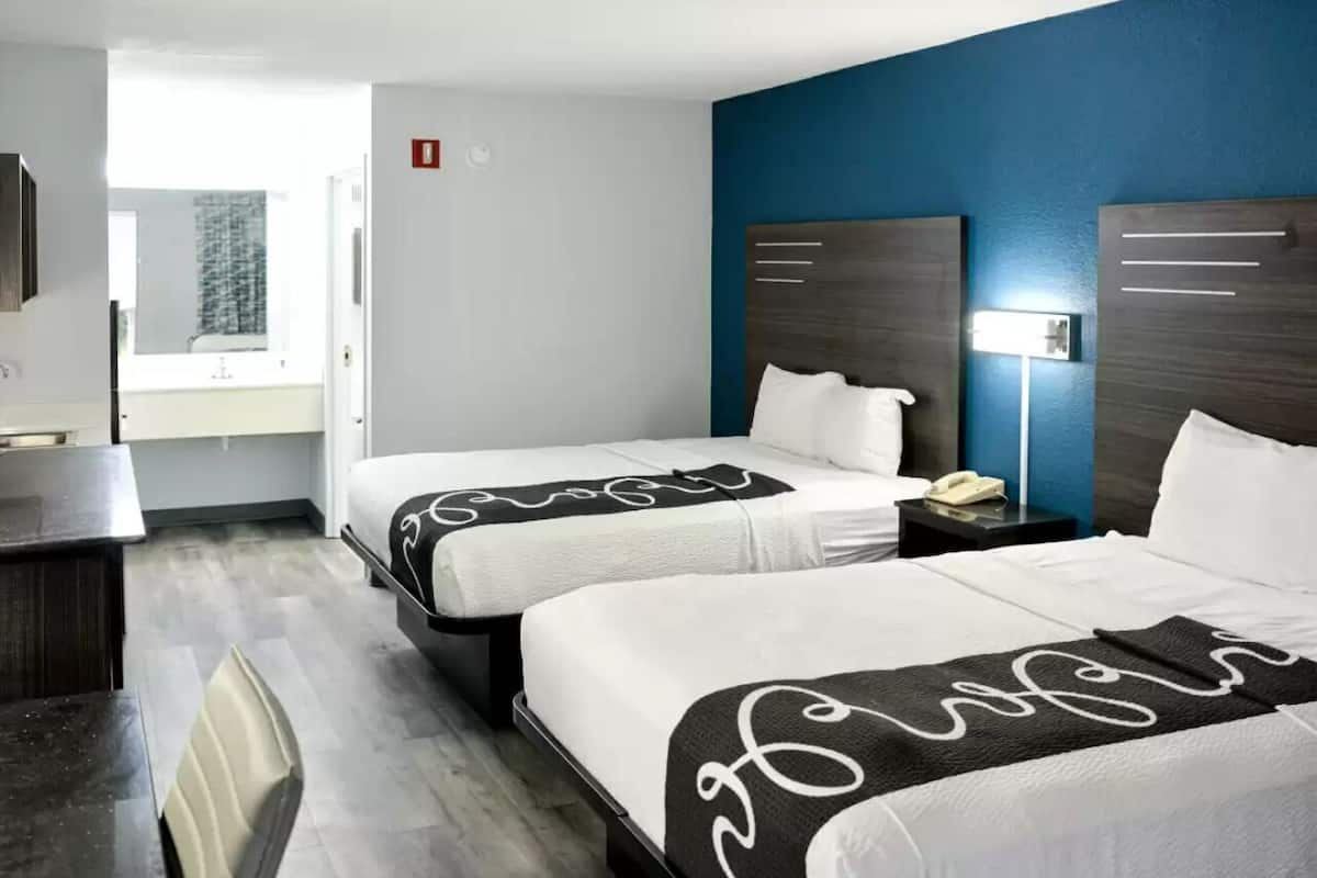 A hotel room with two beds, a desk, and a bathroom visible through an open door.