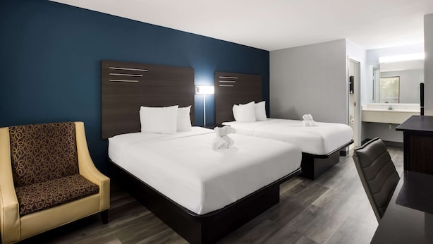 A hotel room with two beds, a desk, a chair, and a bathroom visible through an open door. - Suburban Studios Hinesville - Fort Stewart Area (Hinesville)