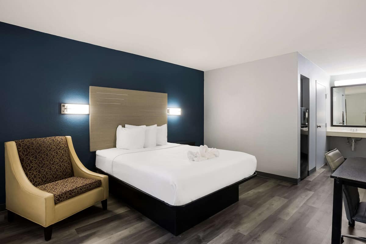 A hotel room with a bed, a chair, a desk, and a mirror.