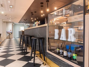 Un espace bar avec un sol à carreaux, des tabourets noirs et une vitrine en verre où sont exposées des bouteilles.