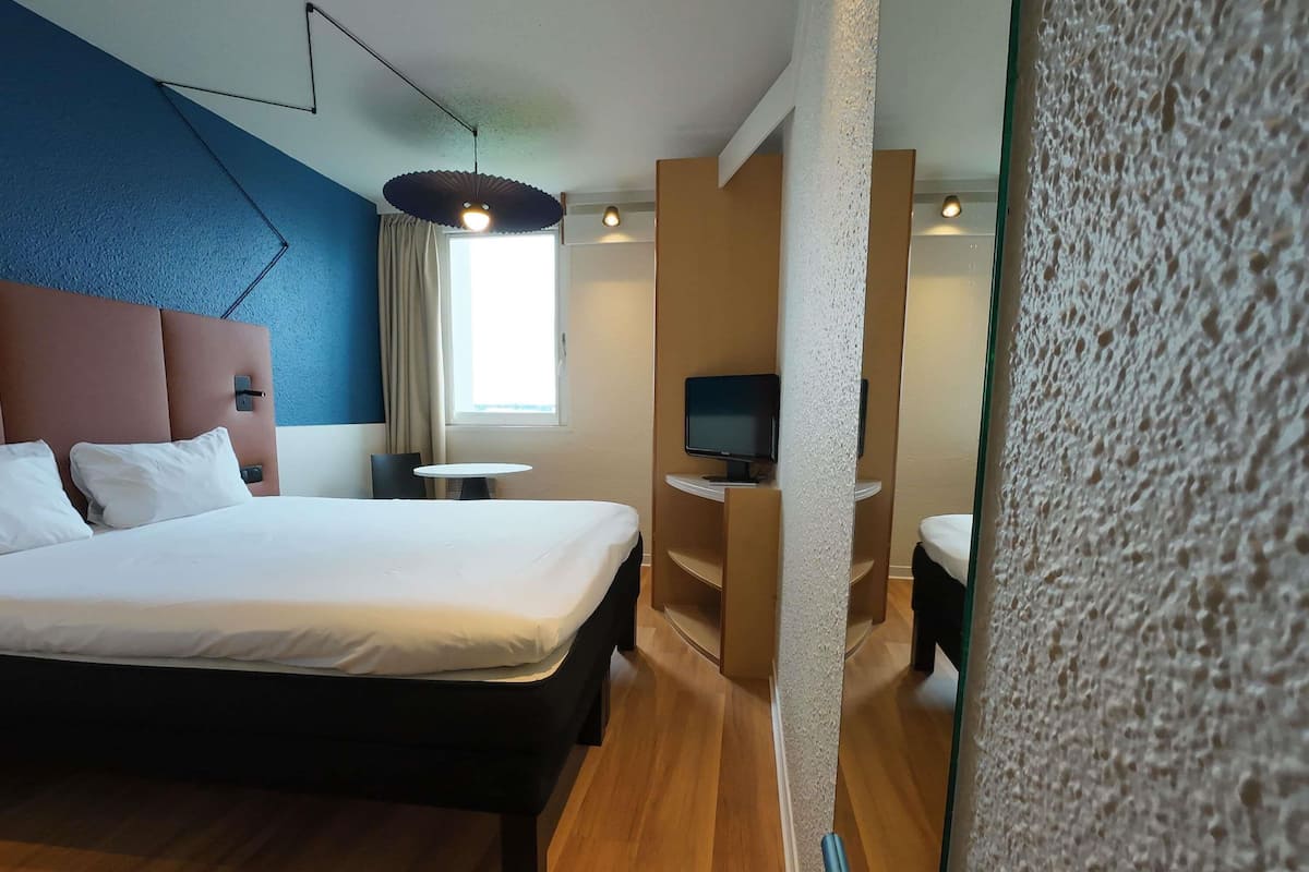 Une chambre d’hôtel avec un grand lit, une télévision, une petite table et une fenêtre avec des rideaux.