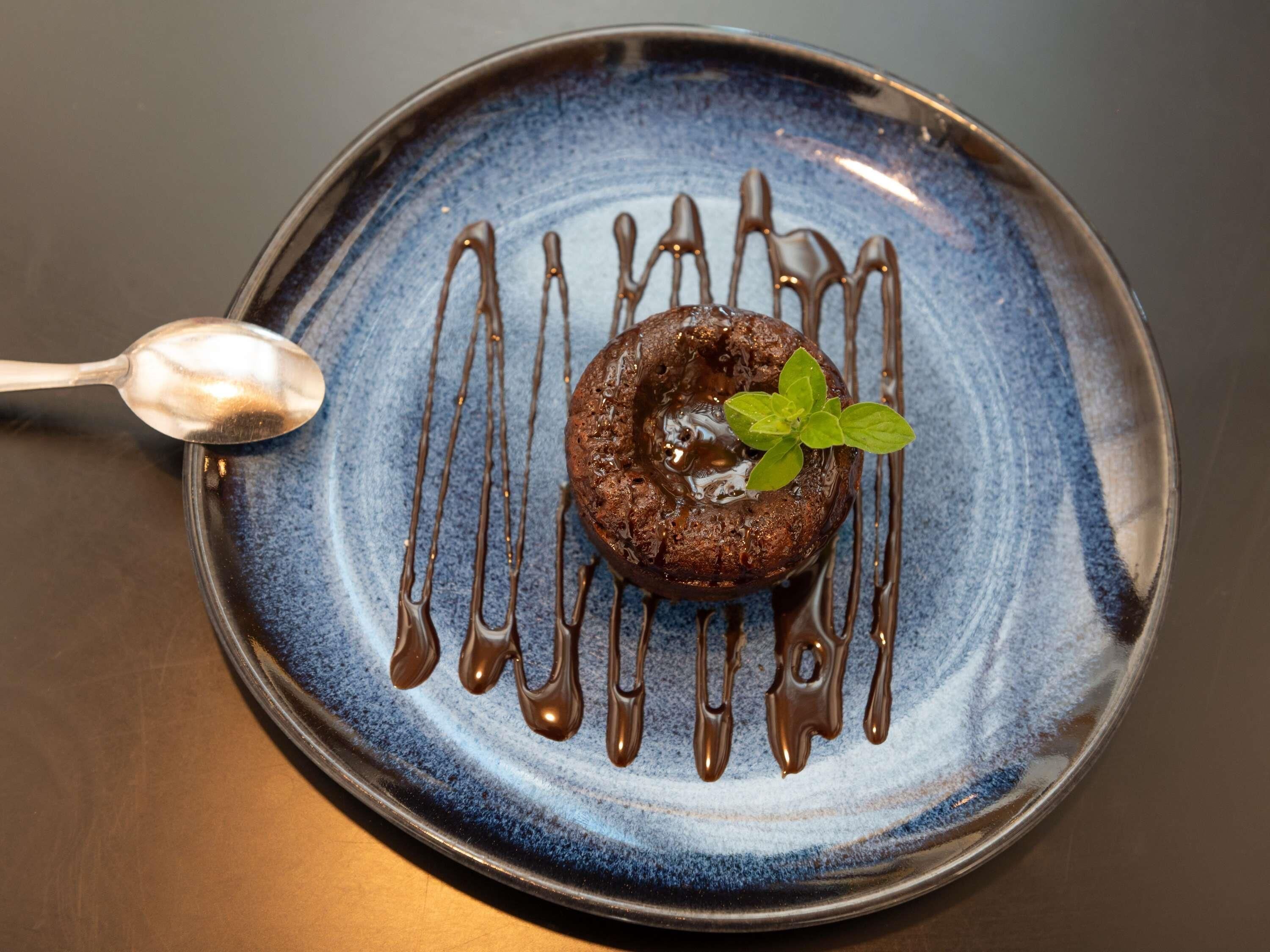 Ein Dessert auf einem blauen Teller, umflossen von Schokoladensauce.