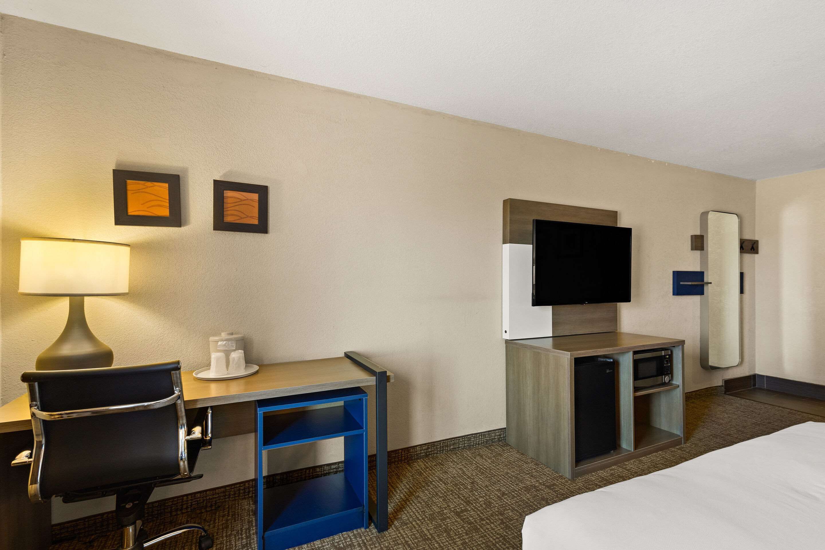 A hotel room with a bed, desk, chair, lamp, television, and a small refrigerator.