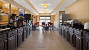 A hotel kitchen with a long counter, multiple coffee machines, and a dining area with chairs and tables. - Comfort Inn Huntington Near University (Huntington)
