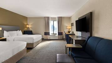 A hotel room with two beds, a sofa, a TV, and a desk.