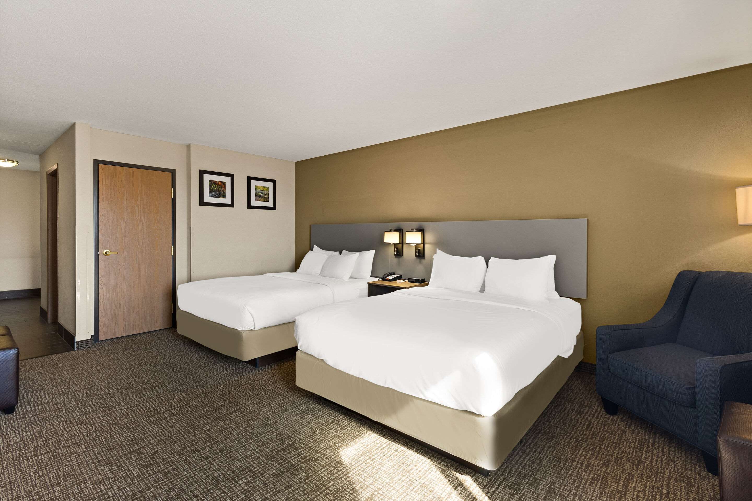 A hotel room with two beds, a desk, a chair, and a door.
