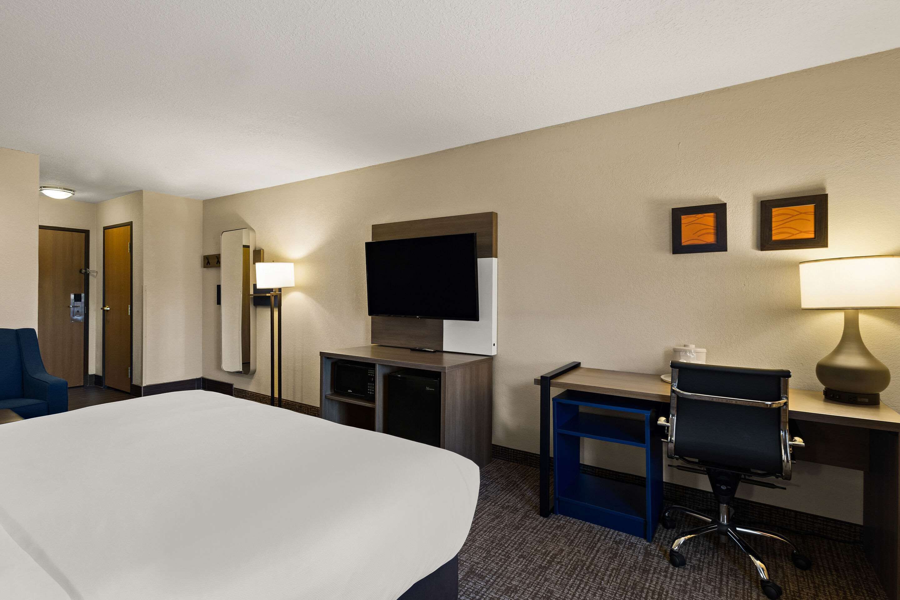 A hotel room with a bed, desk, chair, television, and two framed pictures on the wall.