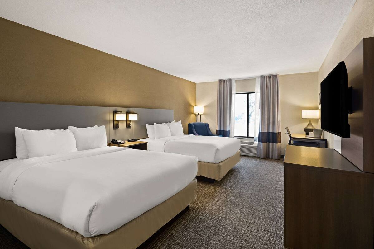 A hotel room with two beds, a desk, a TV, and a window with curtains.