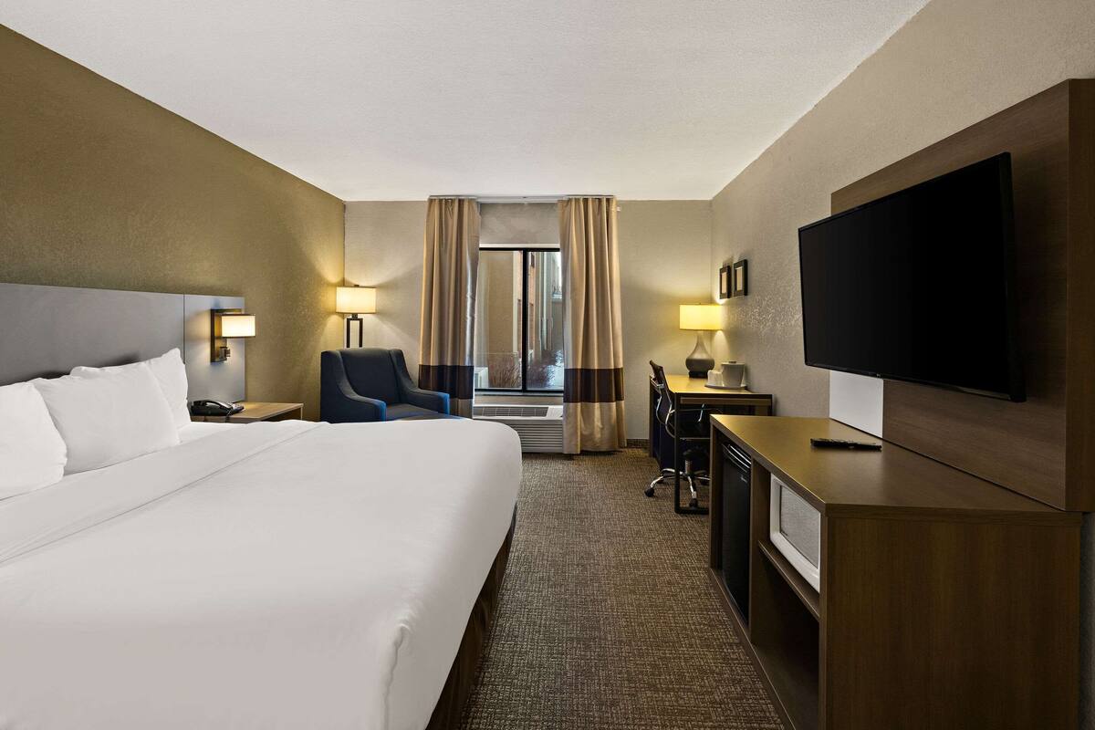 A hotel room with a large bed, a desk with a chair, a TV, and a window with curtains.