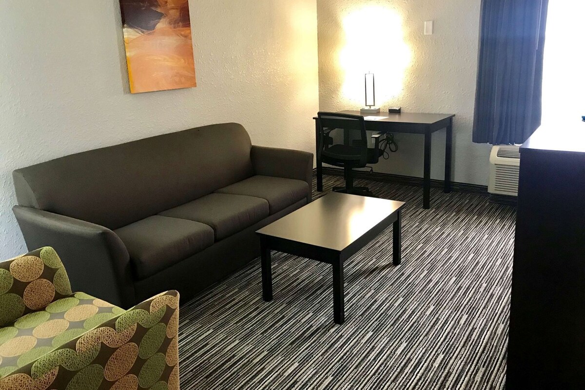 A room with a sofa, a small table, a chair, a desk, and a lamp.