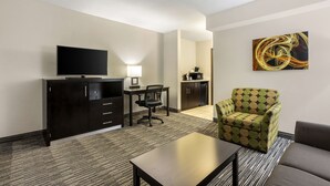 A hotel room with a flat-screen TV, a dining table with chairs, a sofa, a patterned armchair, and a painting on the wall. - Best Western Plus Jonesboro Inn and Suites (Jonesboro)