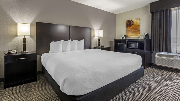 A hotel room with a large bed, two bedside tables with lamps, a flat-screen TV, a coffee machine, and a large window with curtains. - Best Western Plus Jonesboro Inn and Suites (Jonesboro)