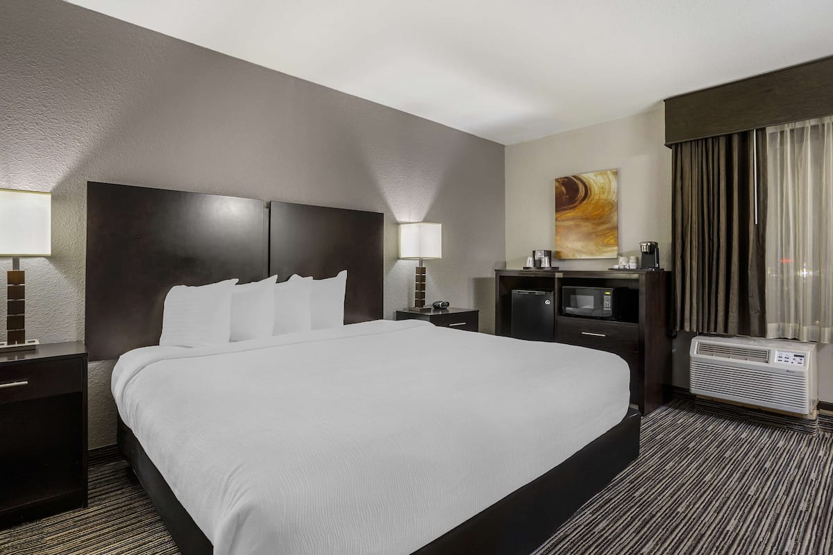 A hotel room with a large bed, a desk with a computer, a microwave, and an air conditioning unit.