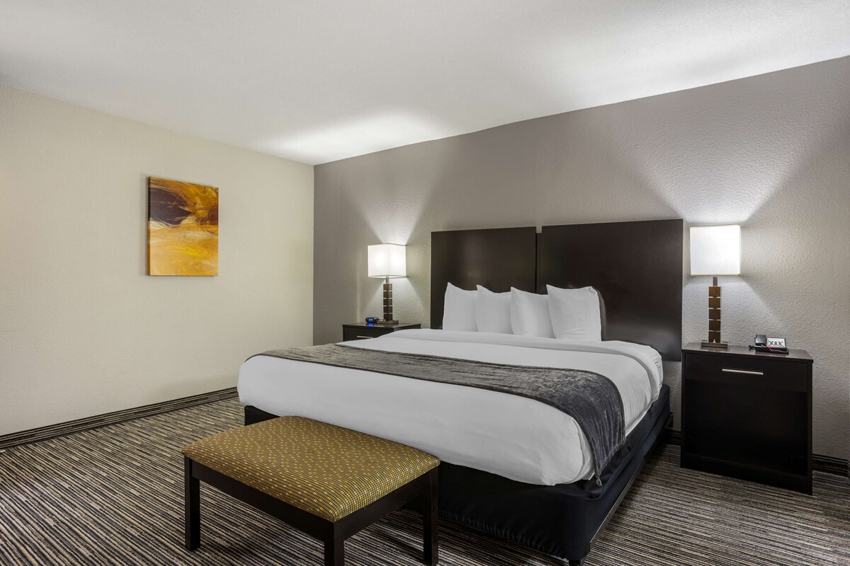 A hotel room with a large bed, two bedside tables with lamps, a bench, and a painting on the wall.