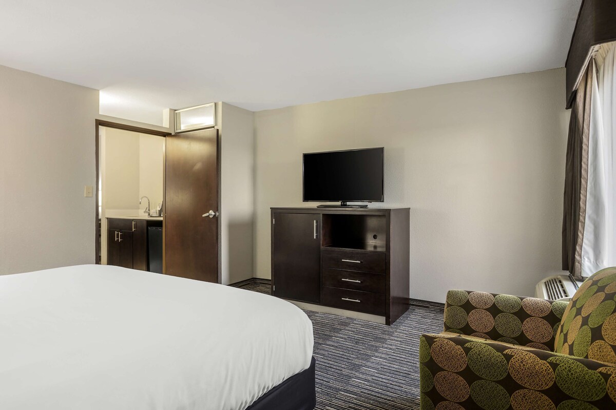 A hotel room with a bed, a TV on a dresser, and a chair.